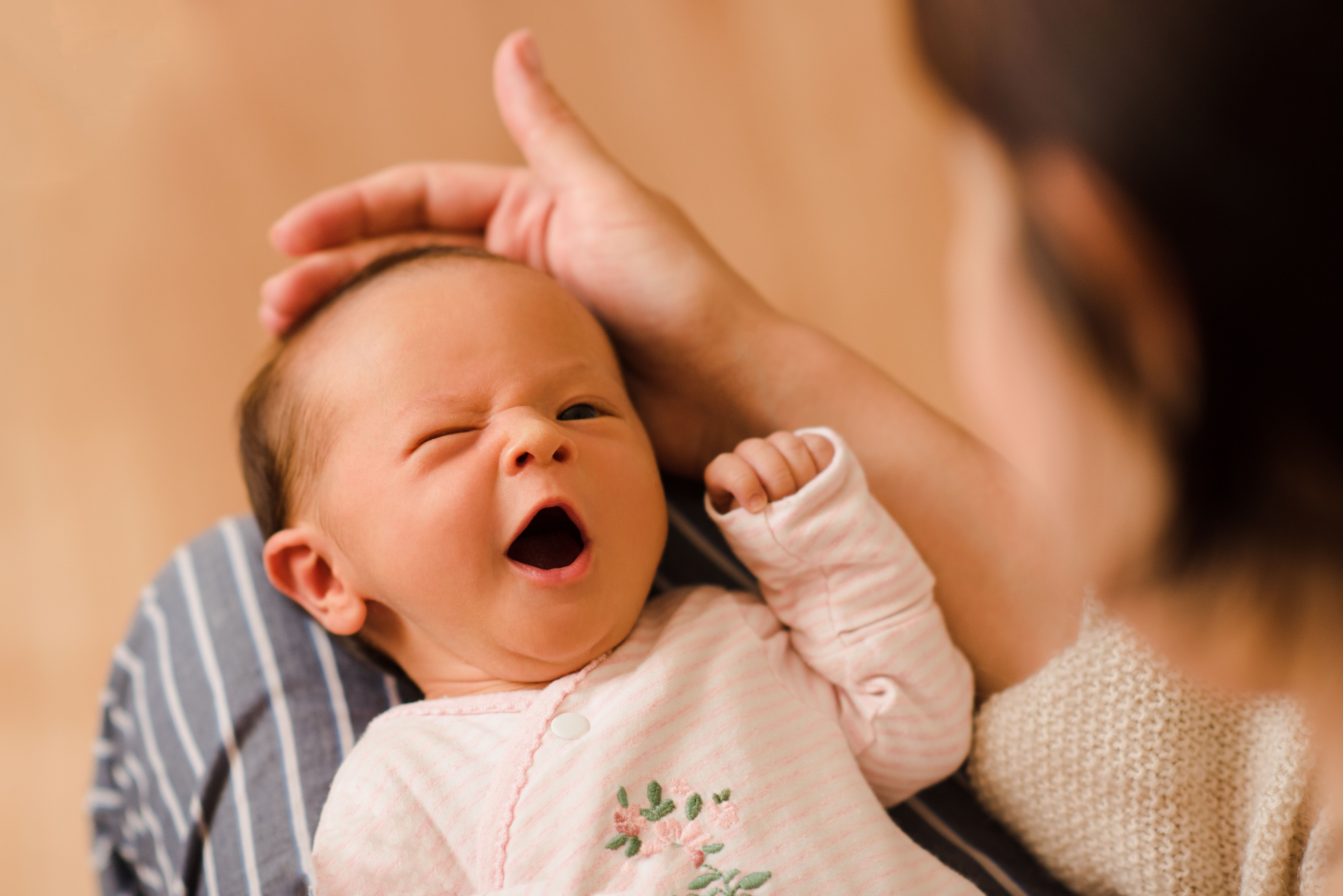 Newborn baby yawning while held by mother